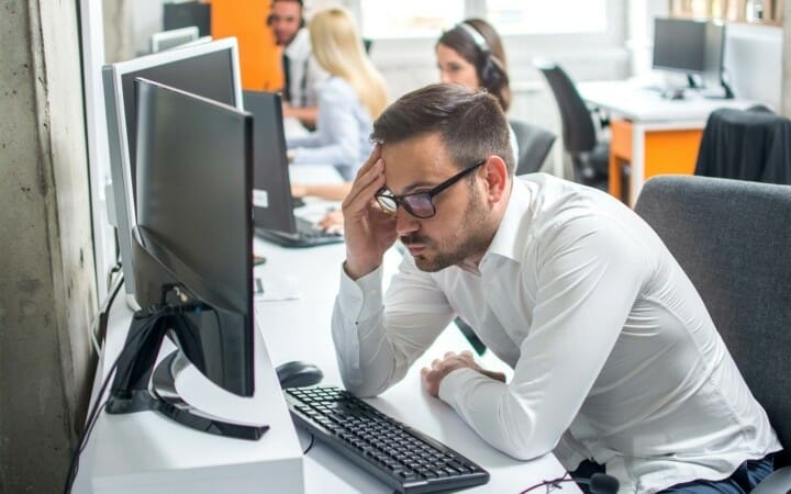 worker looking very frustrated at desk with computer